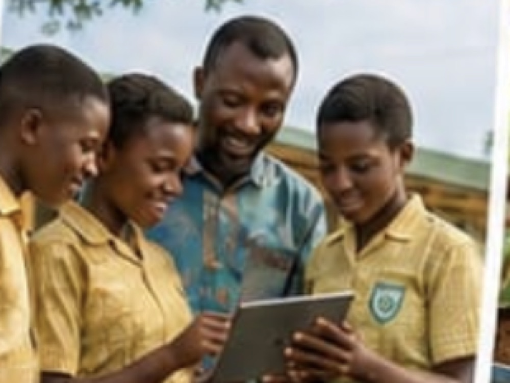 Pupils and a teacher looking together at a tablet, recording tree monitoring data outdoors